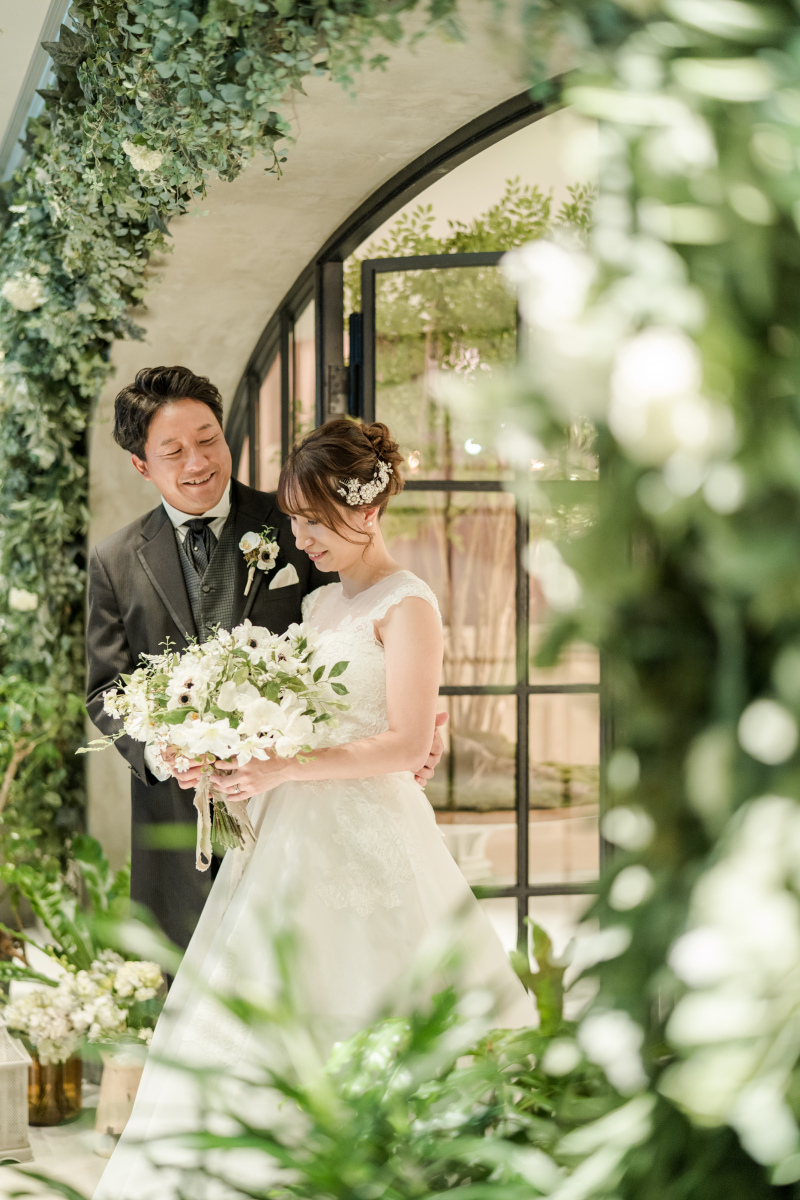 緑に包まれたエントランスでのカット！お二人の優しい表情をとらえた１枚ご新婦さまの横顔を、優しく見つめるご新郎さまの表情からはご新婦さまを大切に想うお気持ちが伝ってくる素敵なカットとなりました。