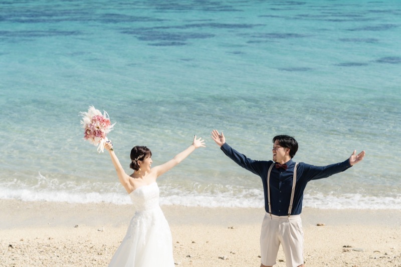 見つめ合いながら、両手をあげる姿。ビーチの青に、おふたりの姿が映える1枚。ピンク色のブーケも可愛らしく、ワンポイントになっています。楽しげな雰囲気が伝わってくるような写真も、大切な思い出になりますよ。