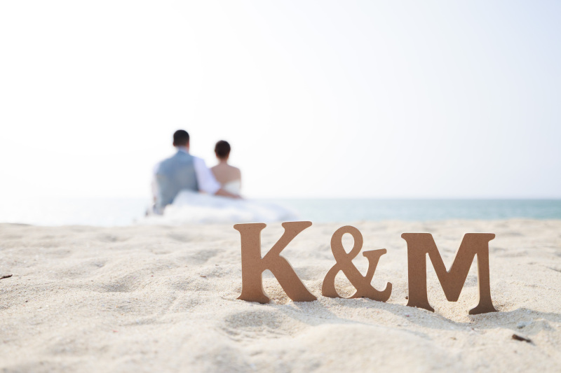 砂浜にイニシャル〈 K ＆ M 〉背景におふたり