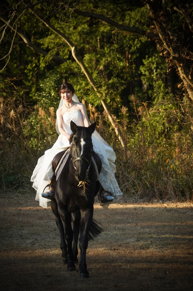 柔らかな光に照らされ、黒馬と進む新婦様の笑顔