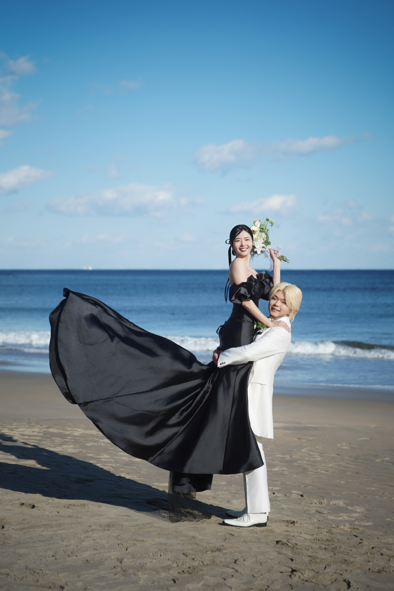 砂浜でふわりと広がる黒ドレスと、弾ける笑顔