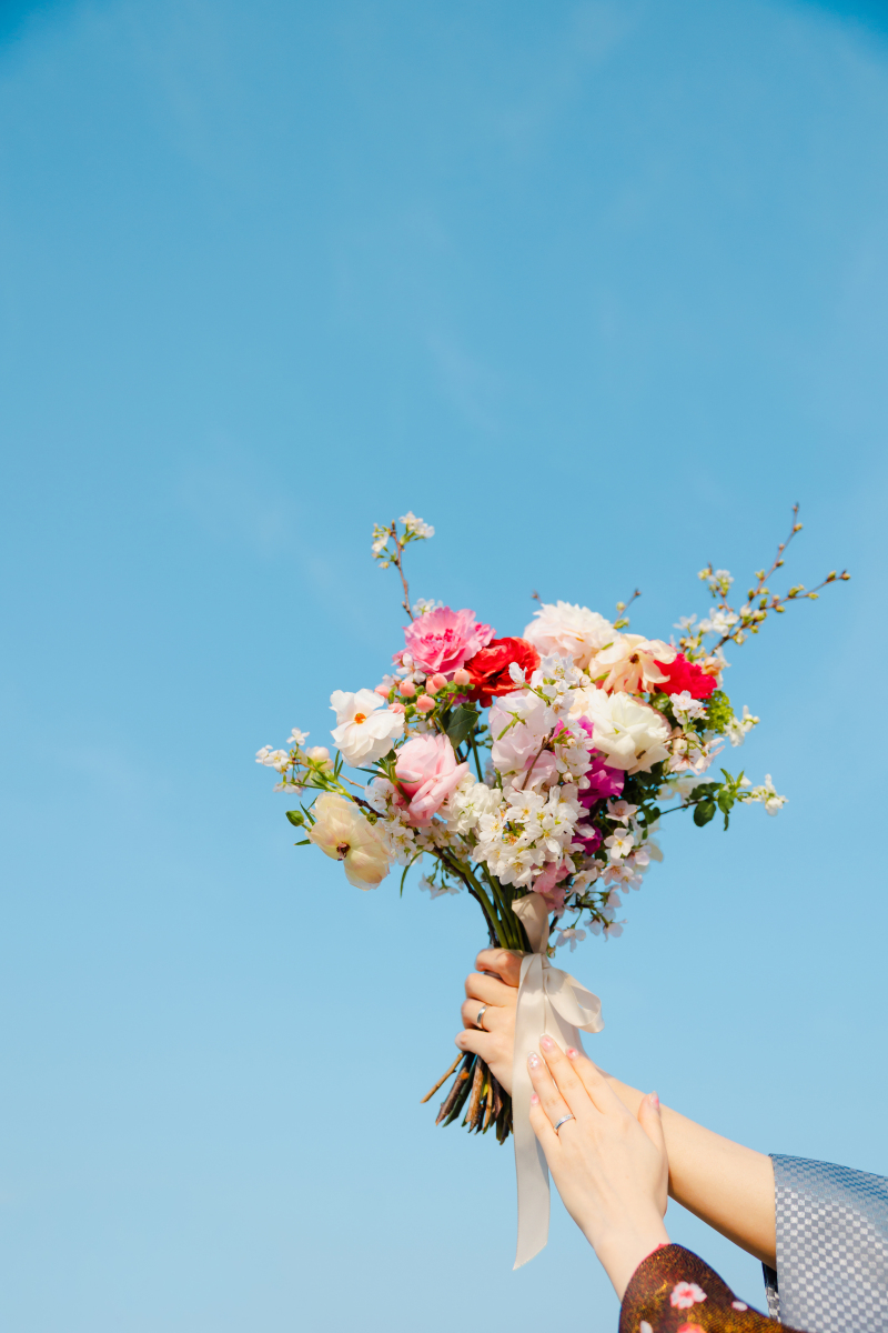 青空を背景に、幸せのブーケを掲げて