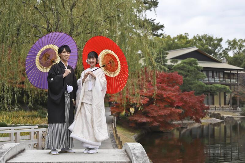 柳と日本家屋をバックに和傘を持って