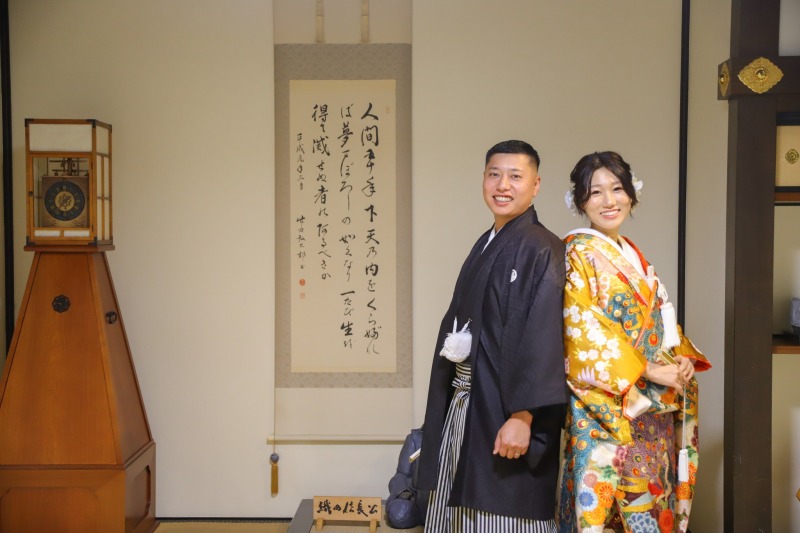 掛け軸と置き時計の前に立つ二人