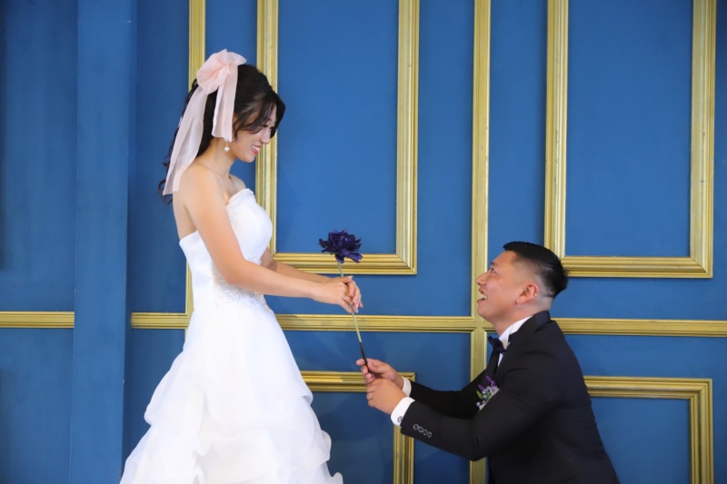 青い壁の前でひざまずく新郎と新婦