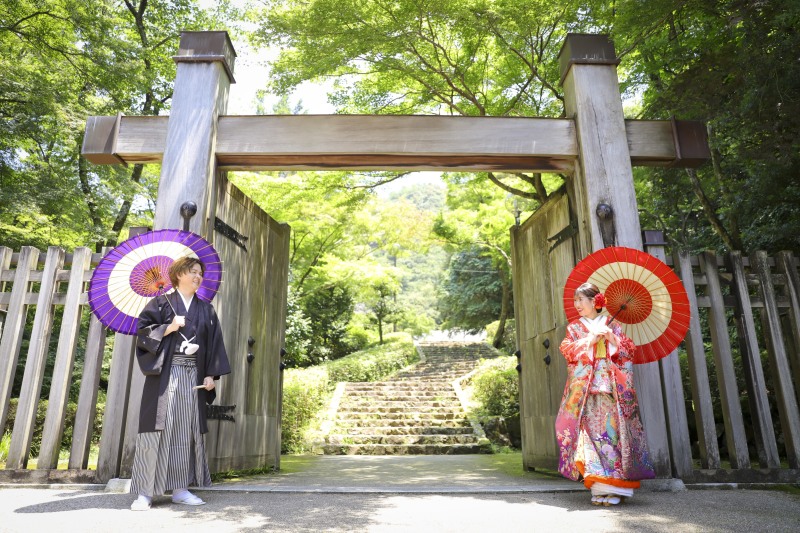 和傘を二人で持って門の前にて