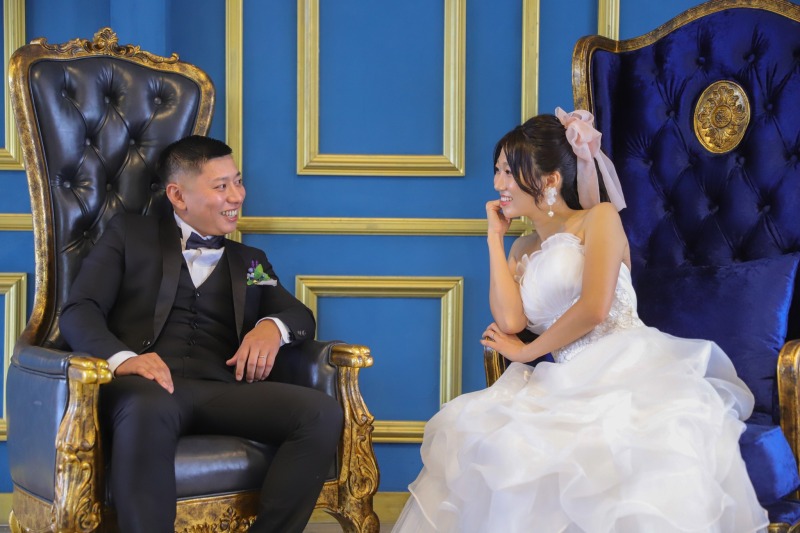 青い壁の前の椅子で向き合う二人