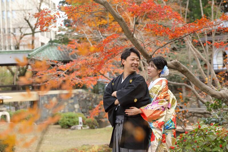 紅葉の名残をバックにニコニコ笑顔で