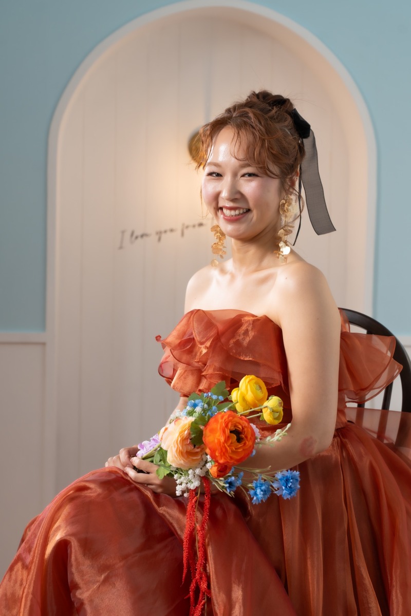 椅子に腰かけ笑うオレンジドレスの新婦