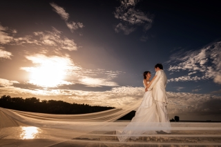 暑さの残る時期での撮影、おふたりの頑張りが沖縄らしい見事なサンセット、素敵な太陽のプレゼントをしてくれました。ロングベールが風になびき、おふたりのお顔も写るドラマティックな特別な一枚に仕上げました。