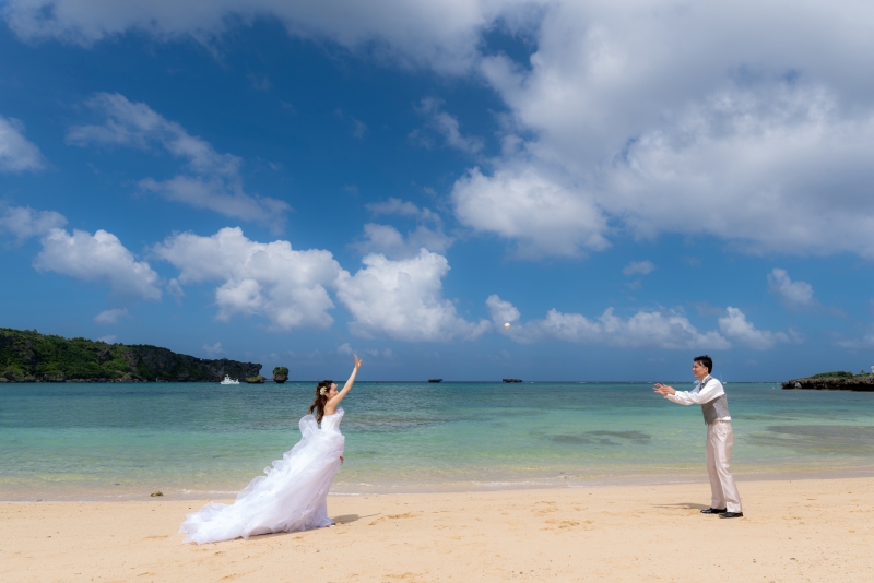 エメラルドグリーンの海と青い空を背景に、ビーチでドレス＆タキシードを着て楽しむキャッチボール。非日常感のフォトウエディングの空間で、日頃のおふたりのなかよしさを感じさせる、自然なショットになりました。