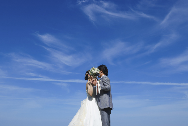 青空の下でブーケ越しに寄り添うショット