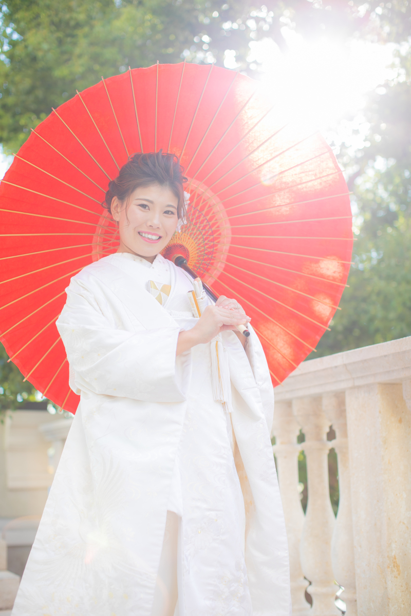 白無垢×赤い番傘は、ご新婦様の白無垢をしっかり際立たせてくれます！グリーンからのぞく陽の光も最高のシチュエーションに！