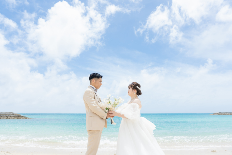 青い海と空を背景にブーケを持ち見つめ合うおふたり