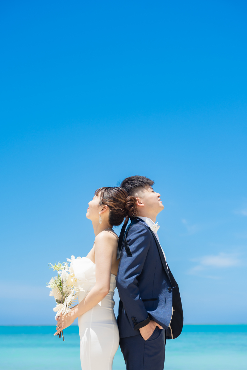 青空と海を背景に背中合わせで立つおしゃれなカット