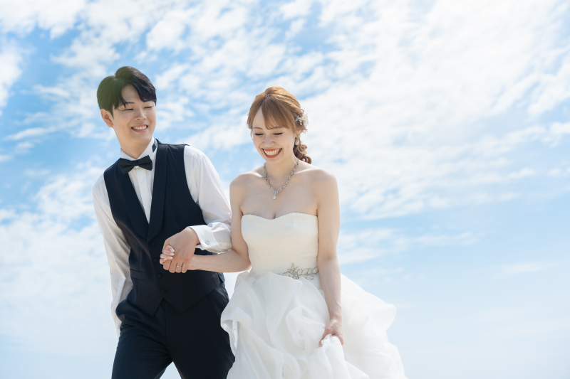 手を繋いで海辺を歩くおふたりの自然体な笑顔が素敵