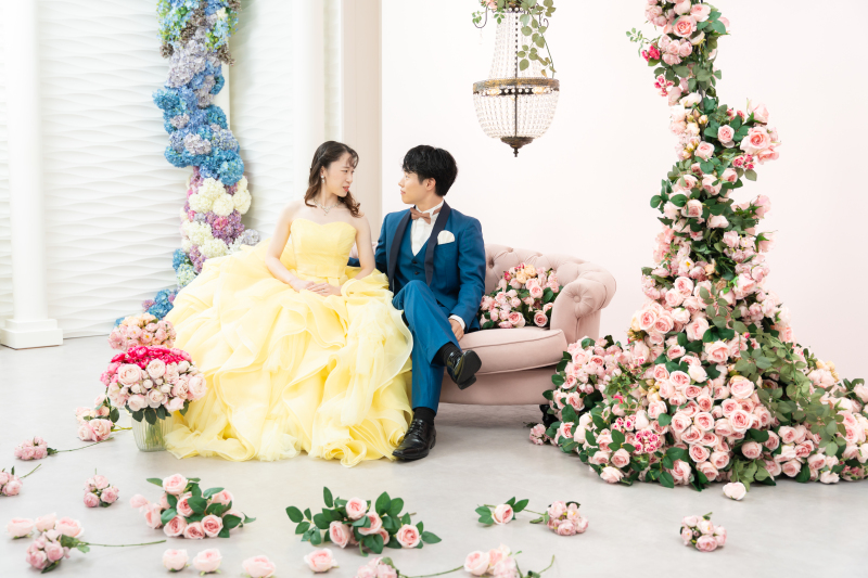 一面の花に囲まれたソファーでお互いを見つめ合う姿