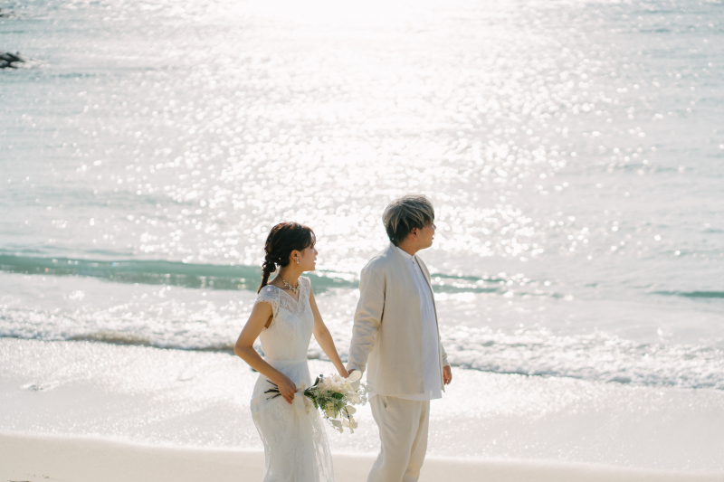 光きらめく海辺で手をつなぐおふたり