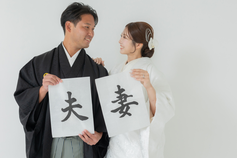 「夫」「妻」の習字を掲げて微笑み合う和装姿