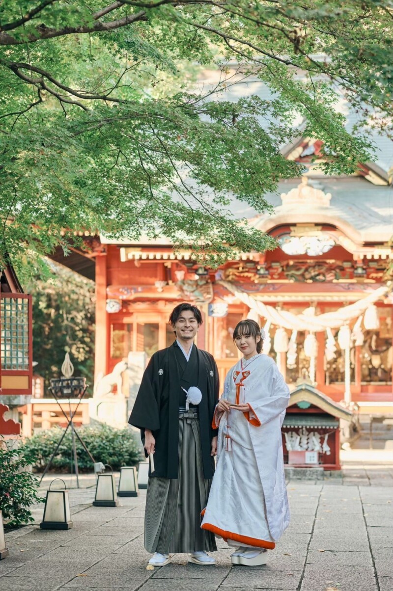 由緒ある神社の本殿を背景にふたりがそっと寄り添う