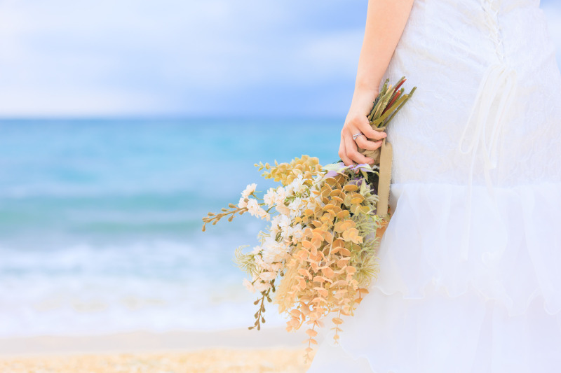 青い海をバックにブーケを持つ手をクローズアップ。