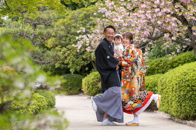 桜と緑にに囲まれた庭園で、笑顔弾けるお二人とお子様。春のあたたかさと幸せを感じさせハッピーな一枚です。