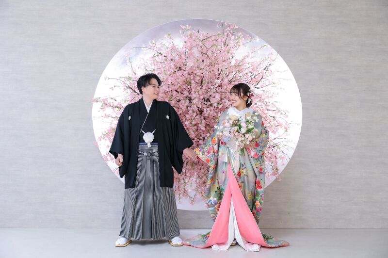桜背景の前で手を繋ぎ微笑み合うおふたり