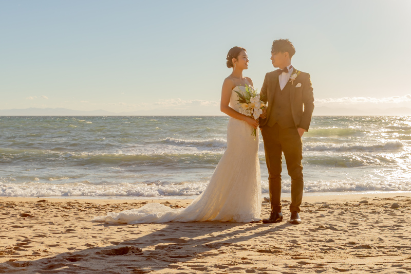 夕暮れの海辺で微笑み合うドレス姿のふたり