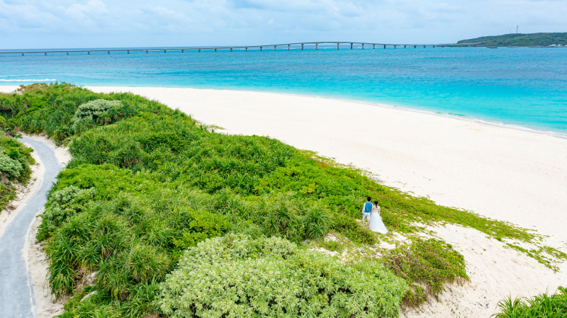 空撮ならではの来間大橋とのカット。澄み渡る青空と、綺麗な海とビーチのコントラストに目が奪われるはず。この場所でしか残せない、おふたりだけの特別な思い出を。