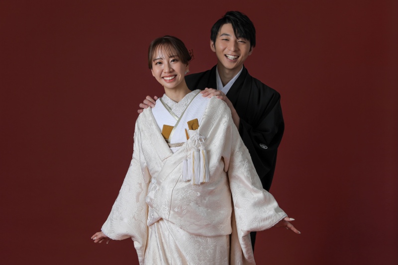 深みのある赤を背景に、白無垢と黒紋付羽織袴が美しく映える和装フォト!寄り添うお二人の笑顔が、温かな絆と幸せなひとときを感じますね❤︎