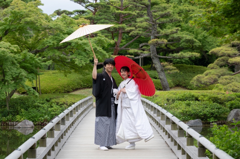 日本庭園の豊かな緑に、白無垢と紋付袴が美しく映える1枚。伝統的な和装に赤と白の和傘を合わせ、橋の上でお茶目にポーズを決めていただきました。お二人の飾らない、幸せいっぱいの笑顔が溢れるカットです。