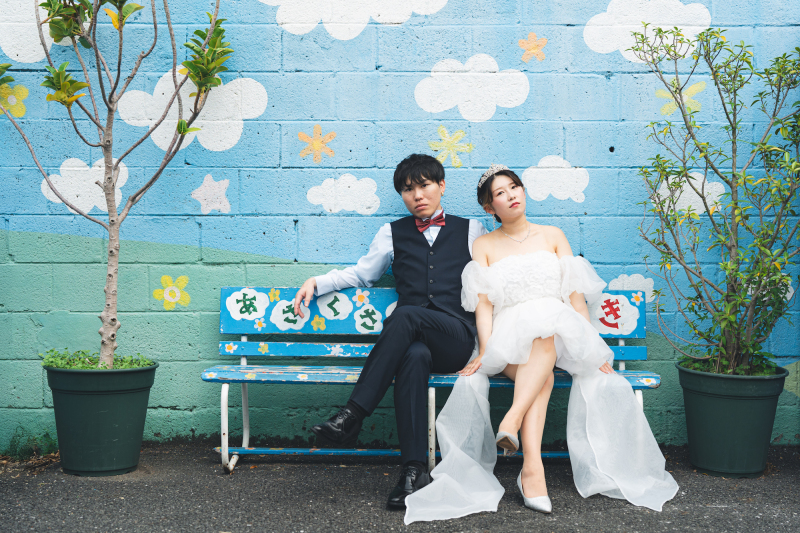 青空のペイントの壁の前で、レトロなベンチに座って