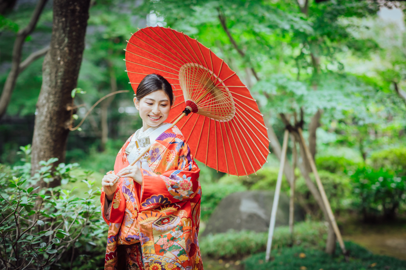 庭園で赤い和傘を差して立つ新婦様
