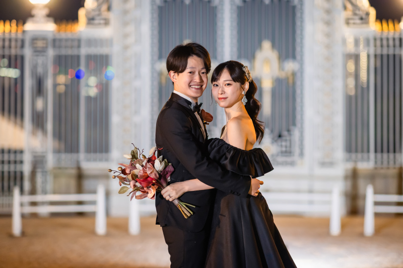 迎賓館の門扉を背にブーケを抱く黒ドレスの華