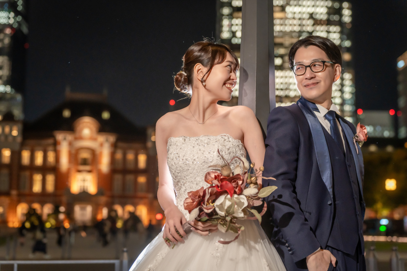 東京駅を背にブーケを持って笑顔のふたり