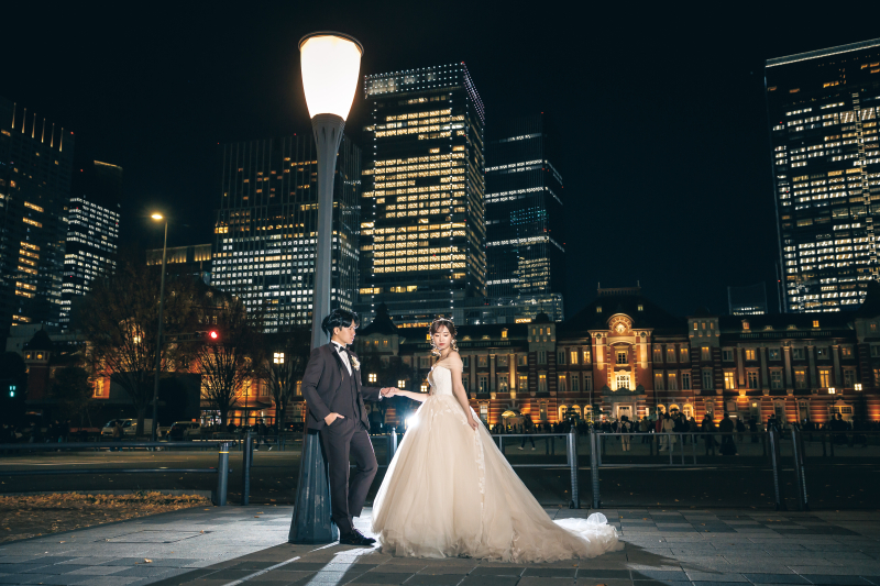街灯を挟んで手を繋ぐスーツとドレスの夜景