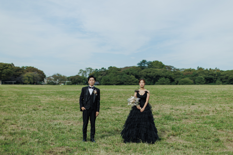 草原に距離を置いて立つ黒衣装の2ショット