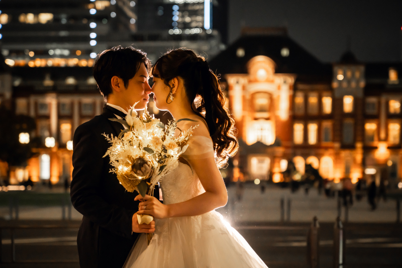 夜の駅舎前でブーケを持ち向き合う新郎新婦様