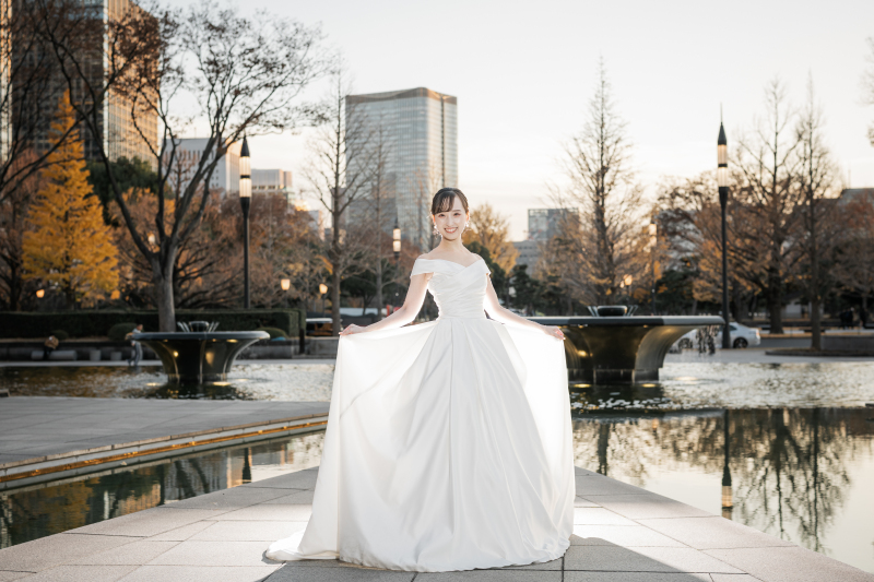 夕景の池を背にドレスの裾を広げて立つ