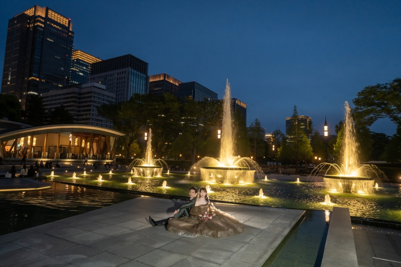 噴水の縁に腰かける夜景に包まれたふたり