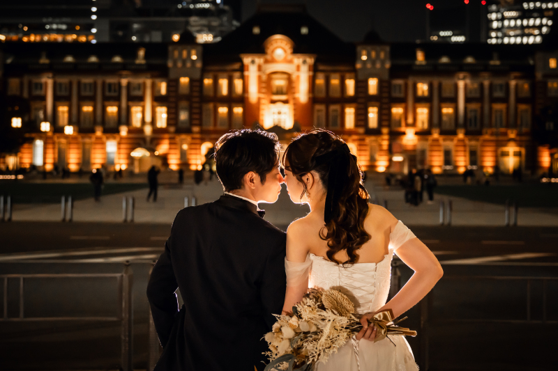 夜の駅舎前で背中合わせに立つ