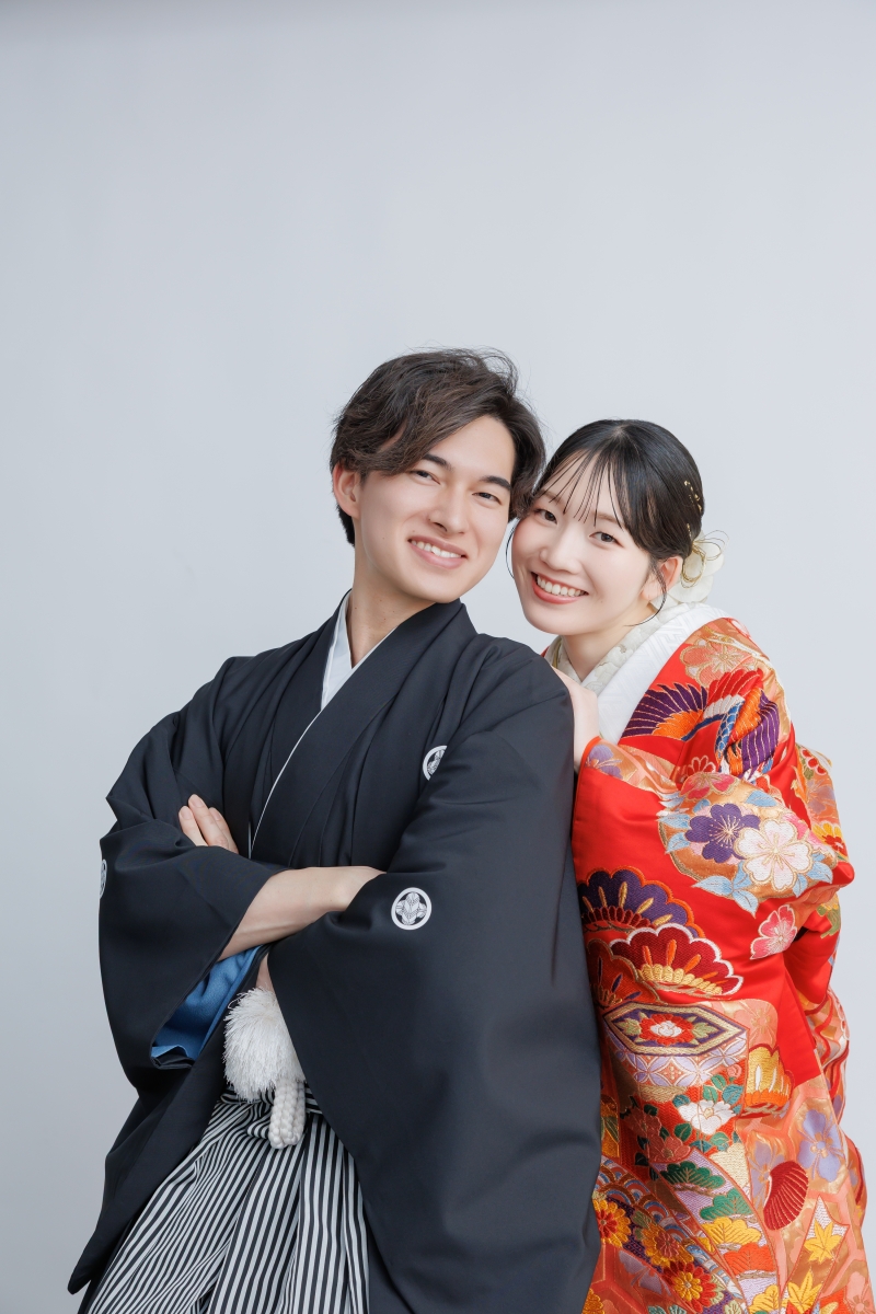 グレー背景に並ぶ黒紋付と赤振袖の笑顔
