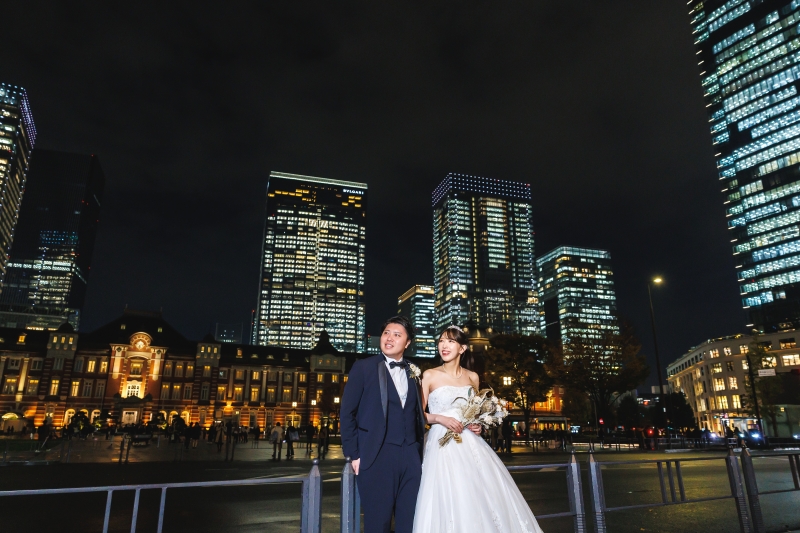 東京駅の夜景の前で並ぶ二人