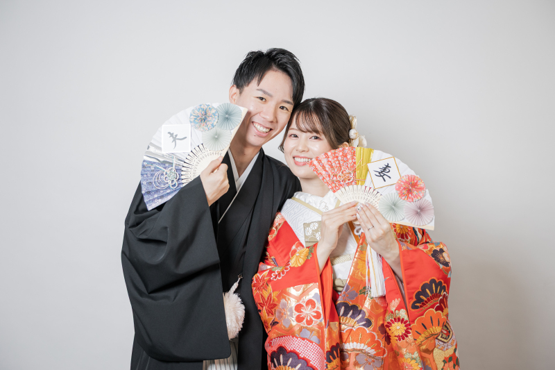 扇子を広げ顔の前に掲げて笑顔を見せる新郎新婦様