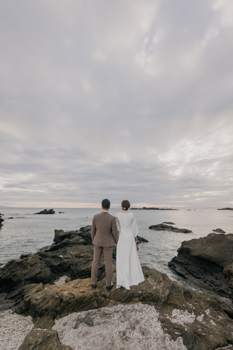 岩場先端で海を背に立つ