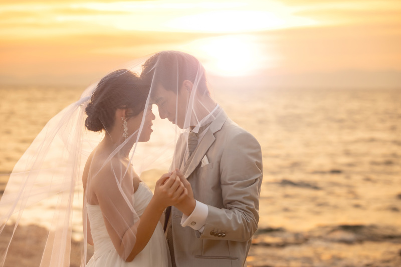 夕暮れの海辺でベール越しに寄り添う洋装写真を残す