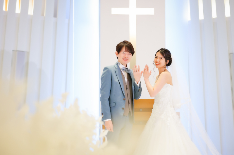 白いチャペルで指輪を見せるおふたりの笑顔の洋装姿
