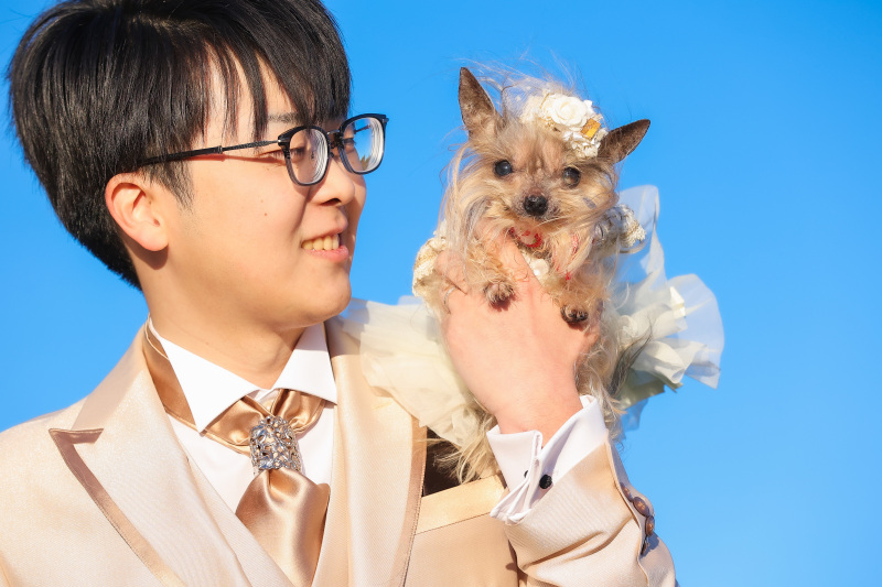 青空の下で愛犬を抱く新郎様のやさしい笑顔の一場面