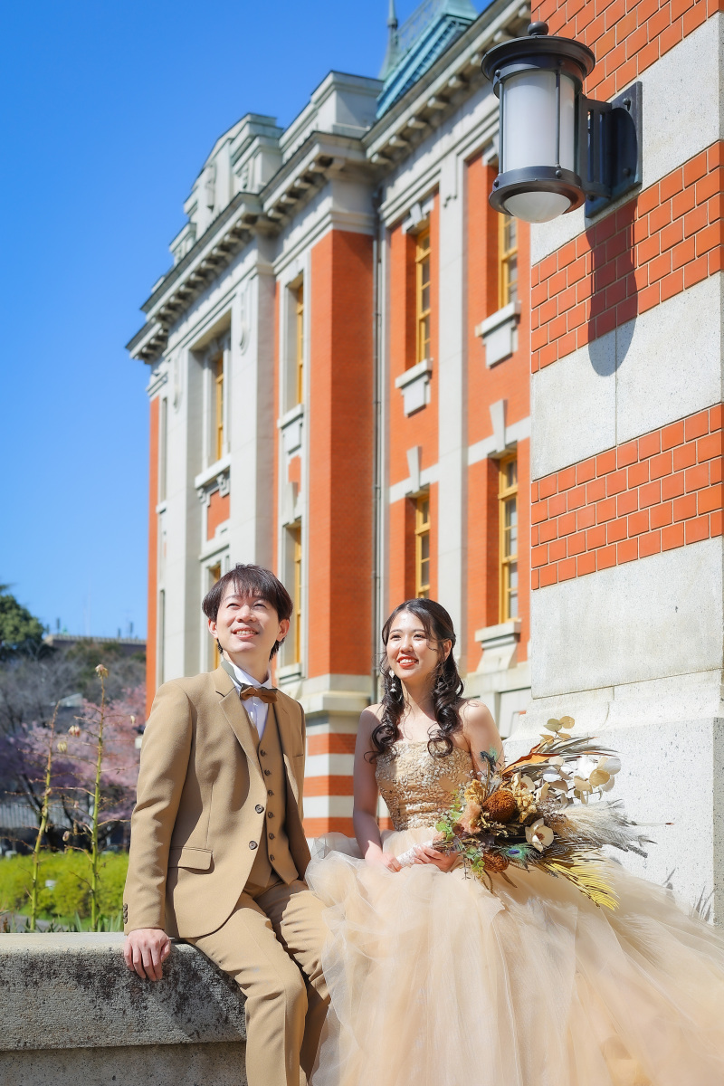 青空と赤レンガに映えるおふたりのカラードレス写真