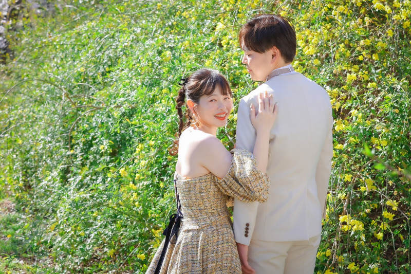 黄色の花に囲まれて寄り添うおふたりの笑顔の洋装姿